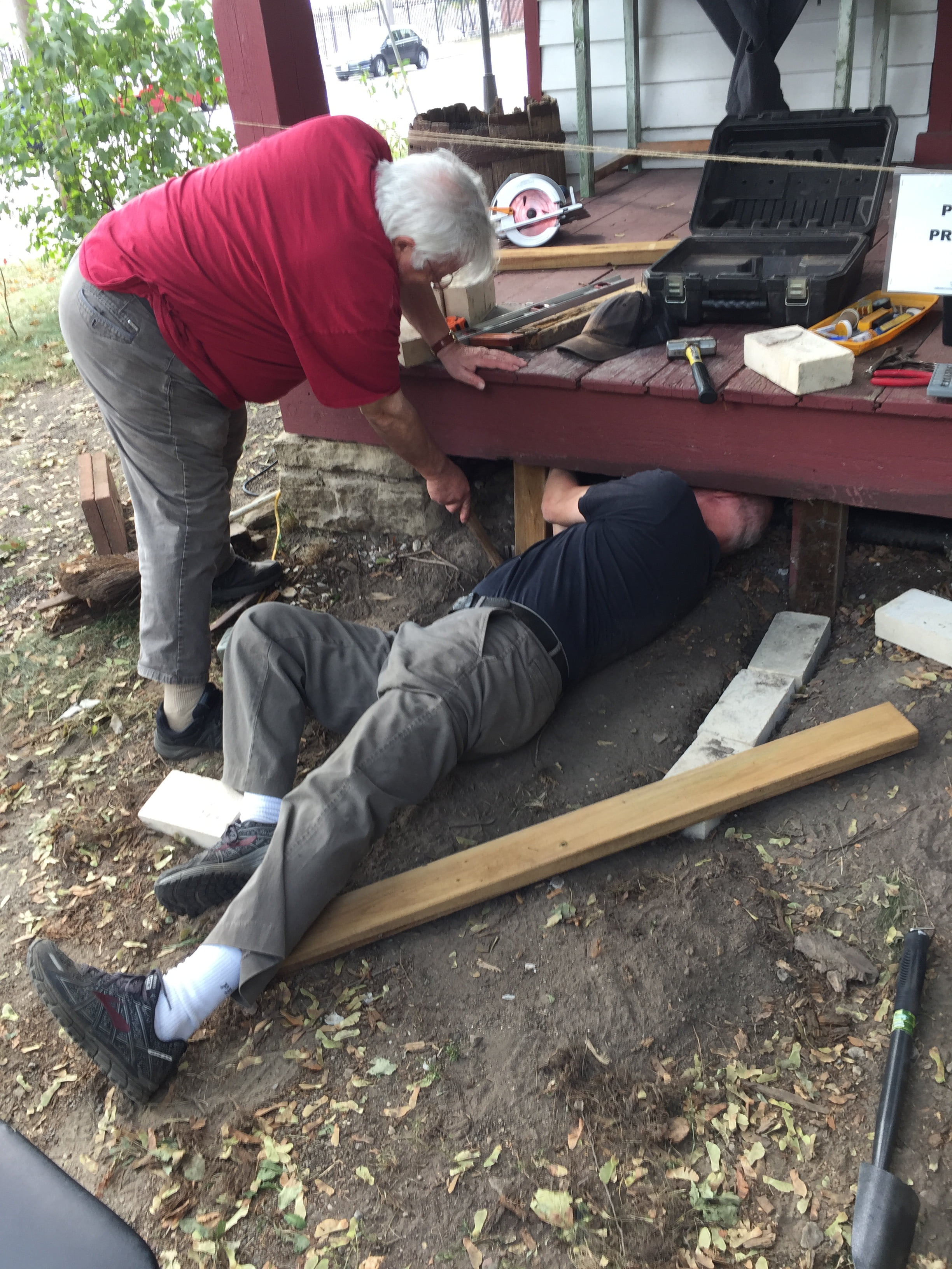 Two volunteers repairing the porch of the Tollkeeper's Cottage, one working underneath it.