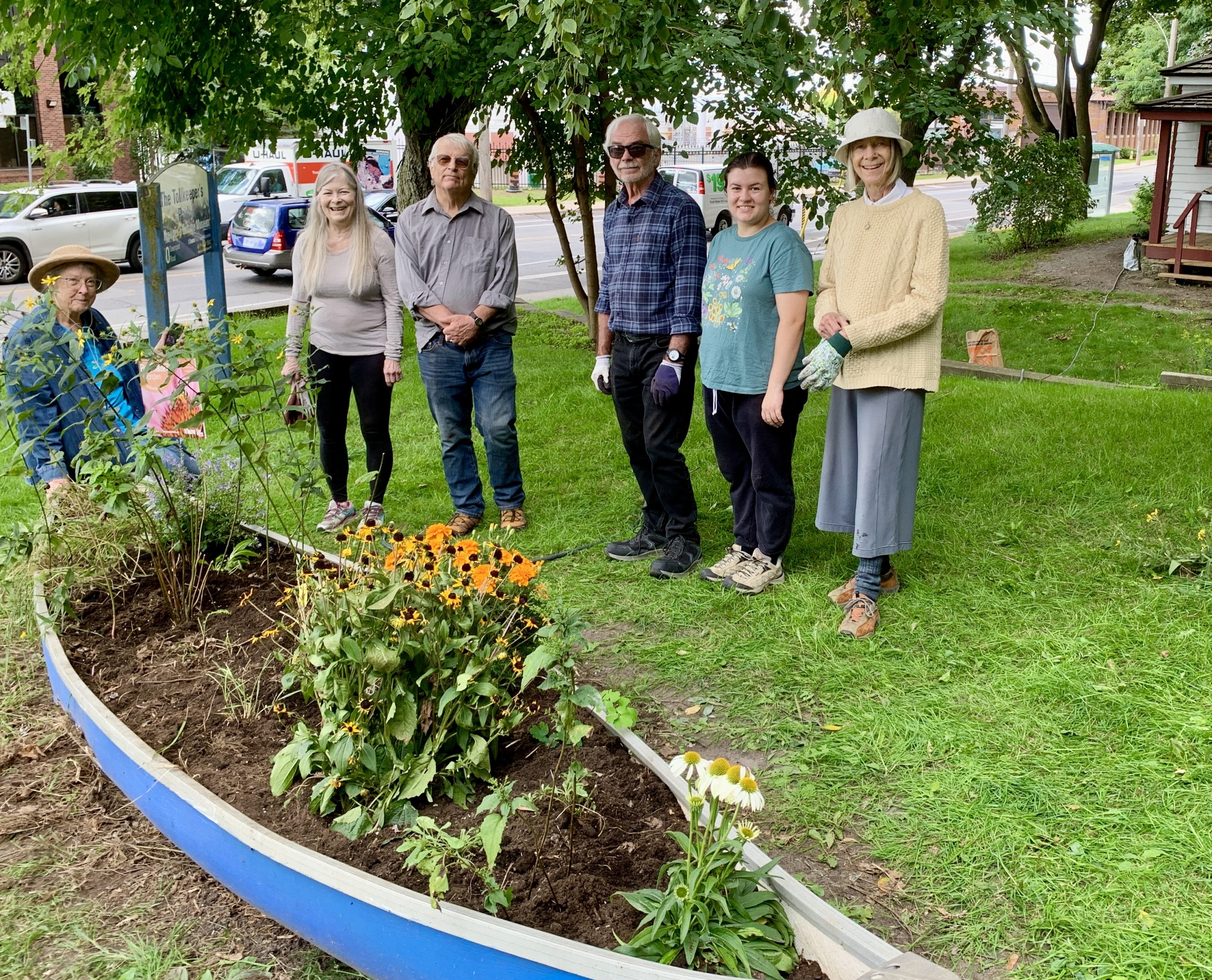 Six volunteers standing beside the canoe planter at the Tollkeeper's Cottage, filled with native flowers.