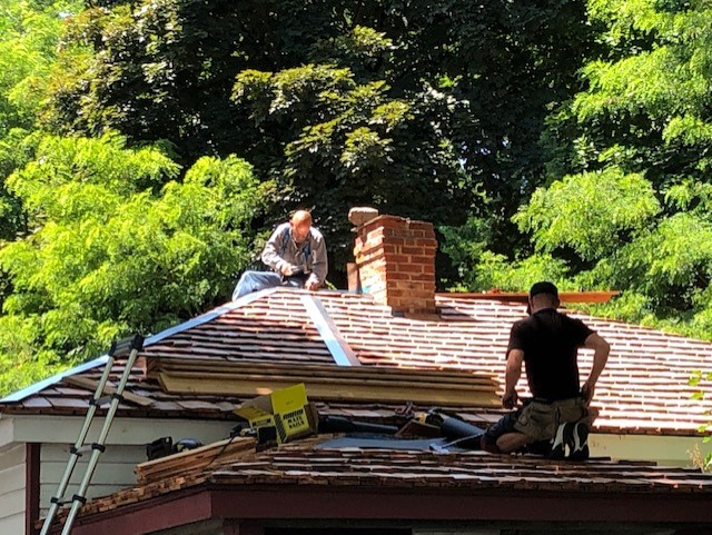 Two roofers stripping shingles from the cottage roof