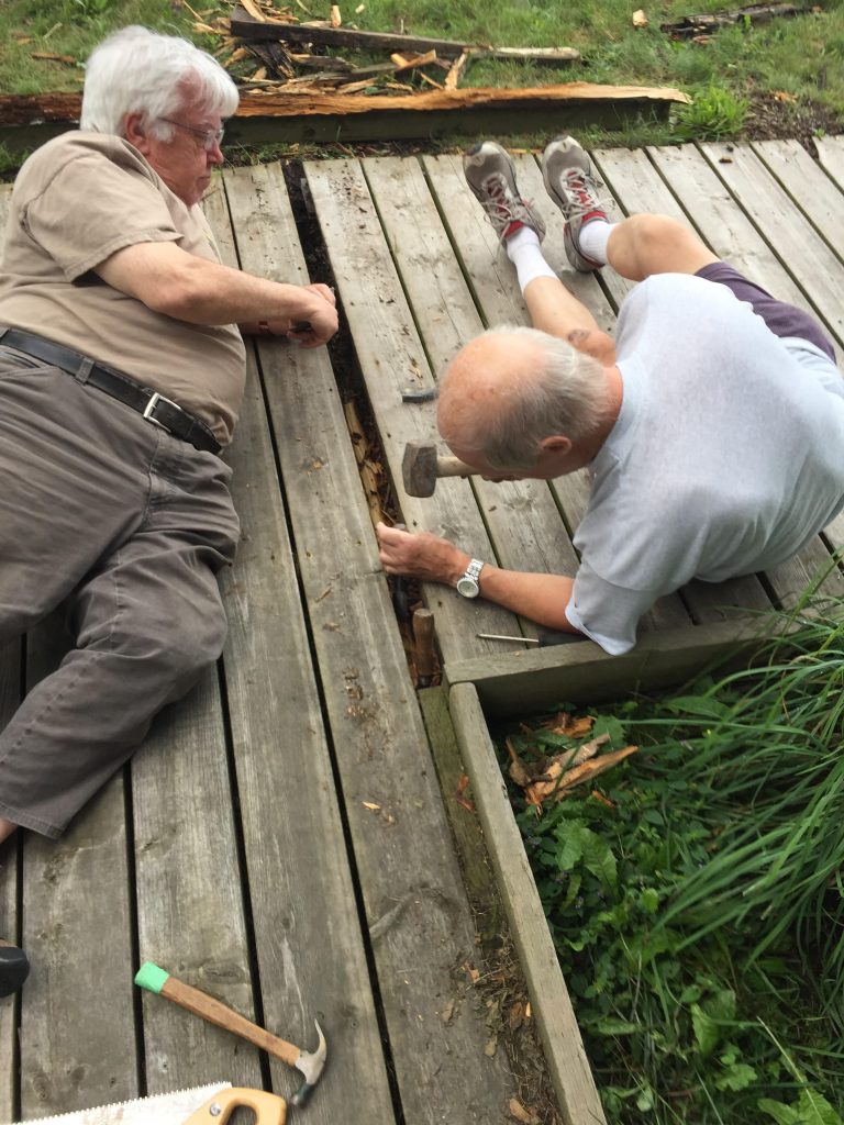 Two volunteers kneeling on the boardwalk, prying up and replacing worn planks